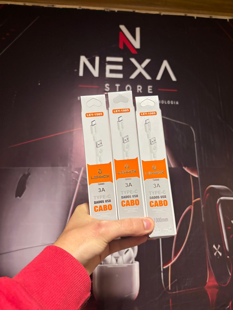 Três unidades do Cabo USB-A para USB-C 3A Lehmox na mão, em frente ao painel da Nexa Store