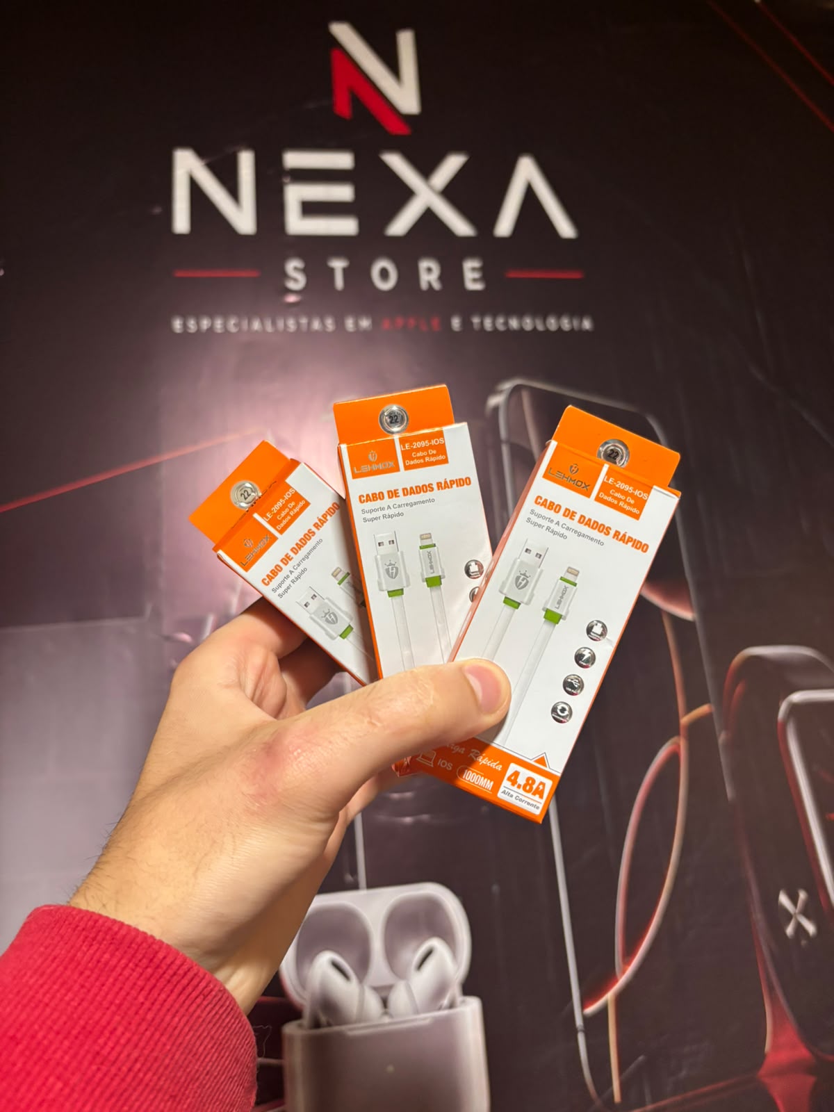Três unidades do Cabo USB-A para Lightning 4.8A Lehmox na mão, em frente ao painel da Nexa Store